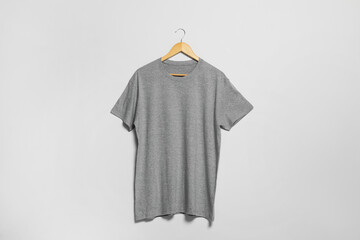 Hanger with grey t-shirt on light wall. Mockup for design