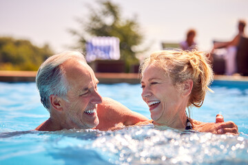 Retired Senior Couple Relaxing In Swimming Pool On Summer Vacation 