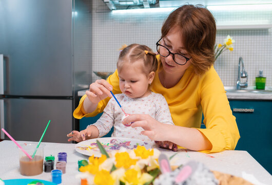 Young teacher woman and little girl are painting Easter eggs at the kindergarten. Concept of education and childish arts