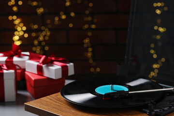 Turntable with vinyl record and Christmas gift boxes against blurred lights, closeup. Space for text