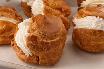Delicious profiteroles with cream filling on table, closeup