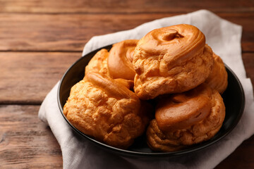 Plate with delicious profiteroles on wooden table