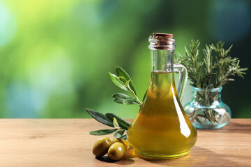 Jug of cooking oil, olives and green leaves on wooden table against blurred background. Space for...