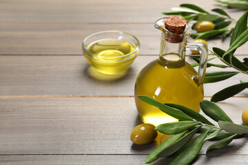 Jug of cooking oil, olives and green leaves on wooden table. Space for text