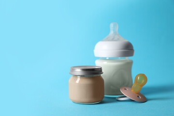 Jar with healthy baby food, bottle of milk and pacifier on light blue background. Space for text