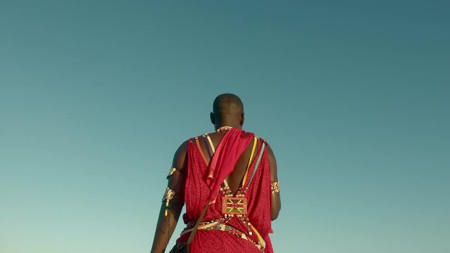 Back View Of An Indigenous Maasai Warrior In Red Traditional Clothes And Tribal Jewelry In Watamu, Kenya. Medium Shot