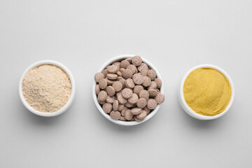 Bowls with different types of brewer`s yeast on light grey background, top view