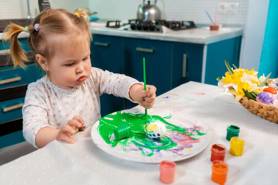 Portrait of cute caucasian toddler girl paintings egg to the Easter. Home celebration