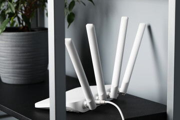 New white Wi-Fi router near potted plant on black shelf