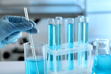 Scientist taking sample of light blue liquid in laboratory, closeup