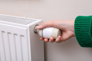 Girl adjusting heating radiator thermostat near white wall indoors, closeup