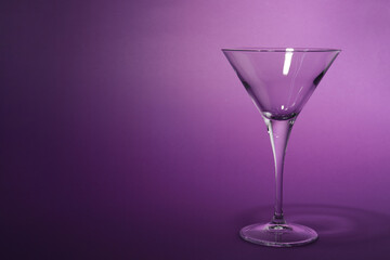 Elegant empty martini glass on purple background. Space for text