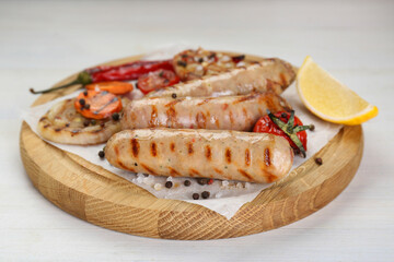 Tasty grilled sausages with vegetables, lemon and spices on white wooden table, closeup