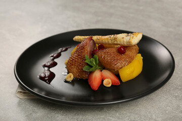 Plate with delicious chicken, parsnip and strawberries on grey table. Food stylist