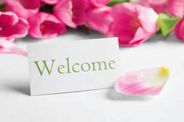 Welcome card and beautiful pink tulips on white table, closeup