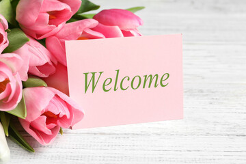 Welcome card and beautiful pink tulips on white wooden table, closeup