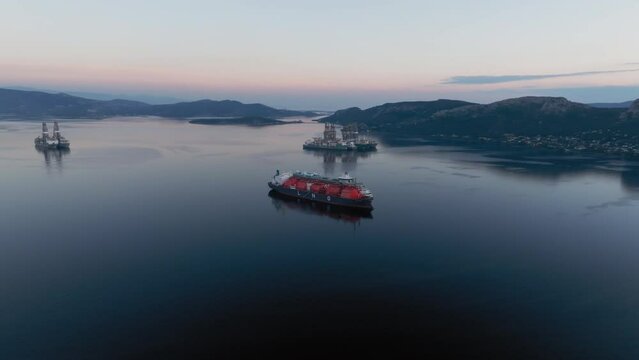 Aerial: Slow panning shot of anchored LNG tanker next to a ferry in calm water during blue hour