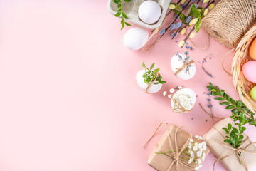 Eco friendly zero waste Easter flatlay. Spring flowers, leaves, eggs on pink pastel background, with craft paper gift box. Woman hands decorate eggs with organic natural decor, preparation for Easter