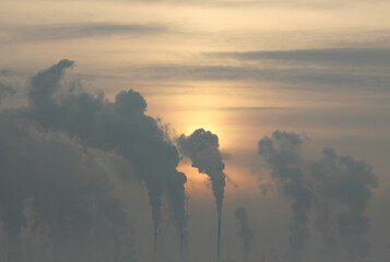 silhouettes of smoking factory chimneys against the background of the rising sun