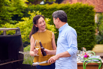 Mature Couple Cooking Outdoor Barbeque And Drinking Wine And Beer At Home