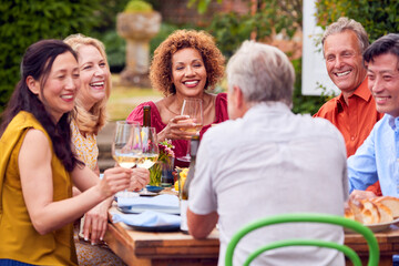 Group Of Mature Friends Talking Around Table At Summer Dinner Party In Garden At Home