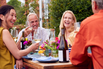 Group Of Mature Friends Talking Around Table At Summer Dinner Party In Garden At Home