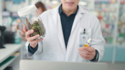 Professional Asian male pharmacists holding medicinal containing cannabis plant extracts at drugstore