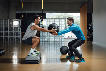 Fitness personal trainer teaching squatting pose while holding medicine ball