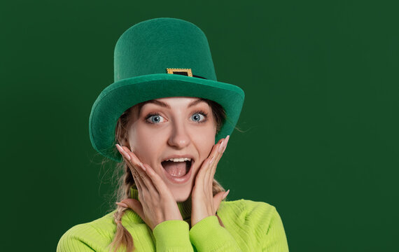 St. Patrick's Day leprechaun surprised model woman in green hat, funny clover shaped sunglasses, isolated on green background and smiling, having fun. Patrick Day party, wow face.