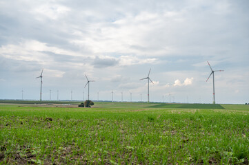 Wind park with a lot of wind turbines during cloudy day, meadow agricultural field in the front