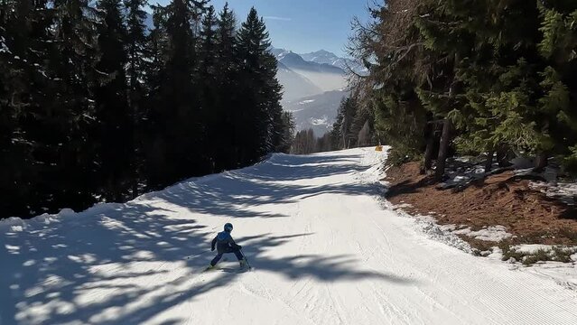 A mother and her child skiing in Bellwald, Switzerland. Beautiful ski resort that runs through the middle of the forest with the ski slope. On the sides are snow lances for snow production