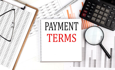 PAYMENT TERMS text on notebook with clipboard and calculator on a chart background