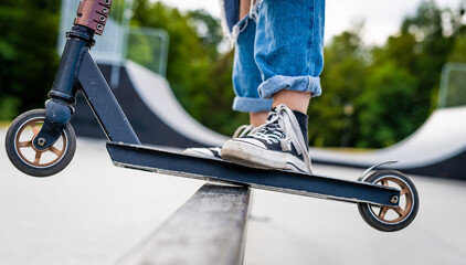 Girl doing tricks on a scooter in a skate park closeup. View on vehicle and person feet.