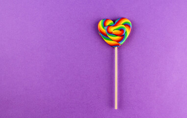 Rainbow colored heart shaped lollipop on purple background