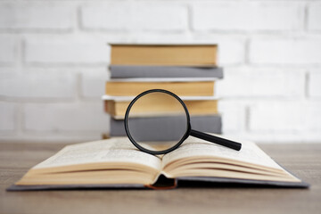 reading, education and research concept - stack of books and magnifying glass on open book in...