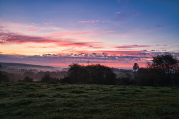 Sunrise over a neighboring forest with meadow in the foreground. Pasture landscape