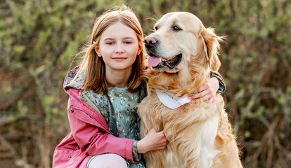 Girl with golden retriever dog outdoors in spring park. Pretty female child kid with pet doggy labrador at nature in sunny day closeup portrait