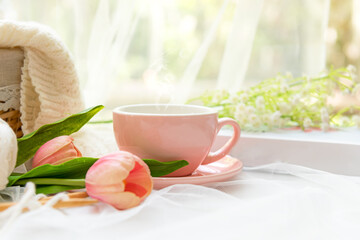 Coffee morning.  Pink steaming cup of hot coffee for relax after working hobbies crochet on white wooden near window with flowers