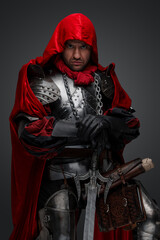 Fototapeta na wymiar Shot of dark knight dressed in steel armor and red robe against gray background.