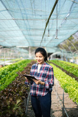 Asian couple of farmers inspects plants with a digital tablet In a greenhouse plantation. Smart farming