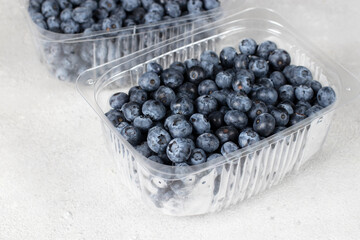 Fresh blueberries in two plastic containers on a gray background, preparing berries for freezing
