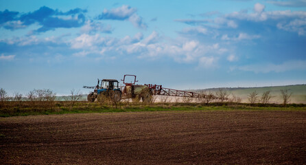 Obraz premium a tractor with a fertilizer sprayer trailer, preparing the land for crops and a beautiful sky in spring
