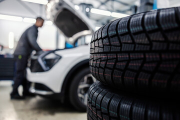 Selective focus on tires with worker fixing car in a blurry background.