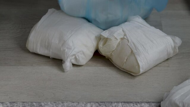 many dirty full baby diapers on floor bed or in blue trash plastic bag,woman hand putting on.small mini trash bin with diapers,carpet room interior.ecology concept,maternity recycle sorting garbage.
