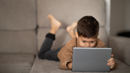 Learning game, app for study. Serious caucasian little child watching video playing on tablet, enjoy rest