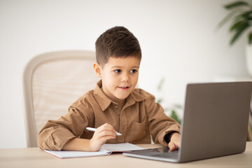Lesson remote, new normal at home. Happy european small kid has video call with teacher, tutor at table