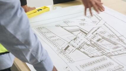 Hand of engineer and architect pointing to building construction design plans on blueprint at site. - Powered by Adobe