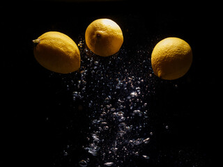Fototapeta na wymiar lemons falling in water with splash on black background