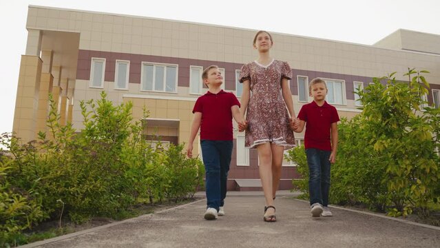 mother leads child sons from school. happy family. children with backpacks after school go home with mom. concept good learning classroom. children after lesson school bag holding mother hand go walk