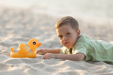HAPPY LITTLE BOY LIES ON A SEA SANDY BEACH AND SMILES